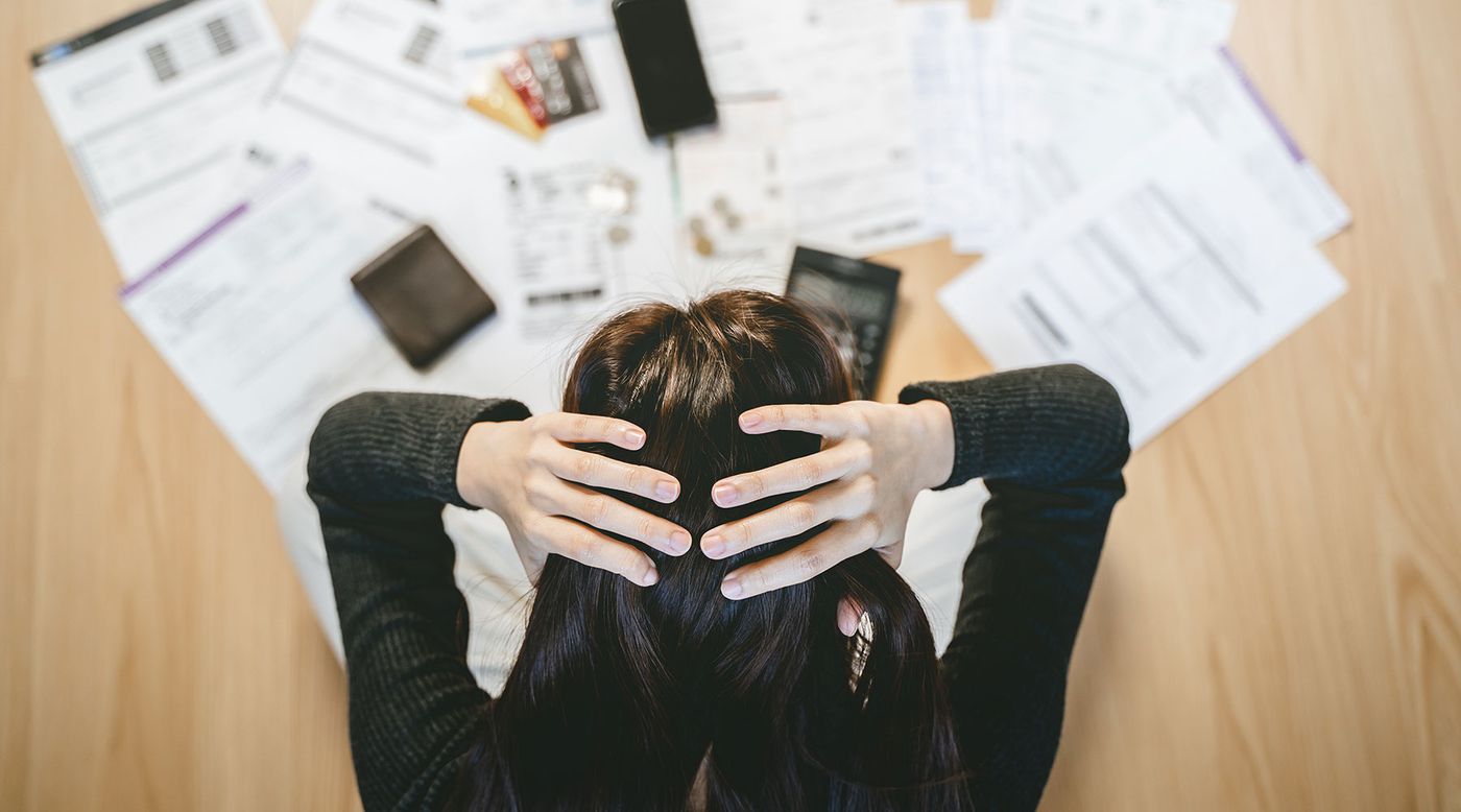 Someone sitting with their head in their hands above a table covered in bills and statements